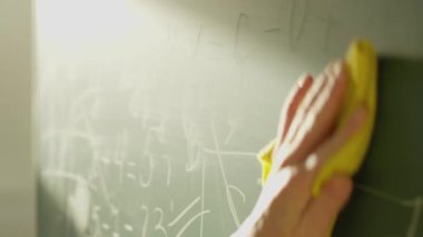 A girl student writes on a green board. Female teacher near the school board. A hand writes information on the board with white chalk. Concept of educational process, demonstration.