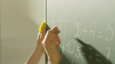 A girl student writes on a green board. Female teacher near the school board. A hand writes information on the board with white chalk. Concept of educational process, demonstration.