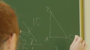 A girl student writes on a green board. Female teacher near the school board. A hand writes information on the board with white chalk. Concept of educational process, demonstration.