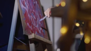 A talented, innovative woman artist paints with a brush on canvas, using multi-colored paints, she creates a colorful, emotional, sensual picture. Modern artist creates abstract modern art. Girl draws