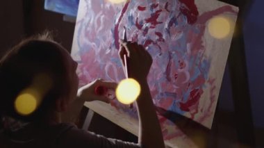 A talented, innovative woman artist paints with a brush on canvas, using multi-colored paints, she creates a colorful, emotional, sensual picture. Modern artist creates abstract modern art. Girl draws