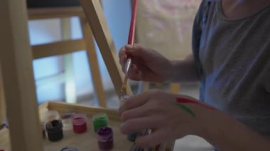 A talented, innovative woman artist paints with a brush on canvas, using multi-colored paints, she creates a colorful, emotional, sensual picture. Modern artist creates abstract modern art. Girl draws
