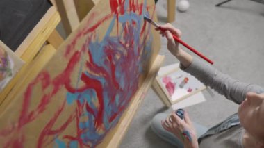 A talented, innovative woman artist paints with a brush on canvas, using multi-colored paints, she creates a colorful, emotional, sensual picture. Modern artist creates abstract modern art. Girl draws