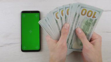 Smartphone green blue screen, man counting dollars cash. Paper money and mobile phone chroma key. Hands hold American dollars, put on table. Banking, work and earnings Internet online and business
