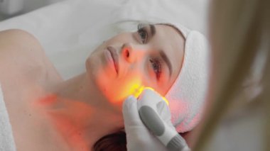 Red LED treatment. Woman doing facial skin therapy. Radiofrequency face lifting. Hardware antiaging procedure. RF lifting and vacuum massage. A cosmetologist performs a cosmetology procedure