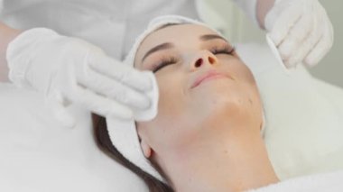 A cosmetologist applies a cosmetic mask to a womans face in a beauty spa. A rejuvenating, restorative and moisturizing procedure for girl on skin of the face in beauty clinic. Relaxation and care.