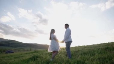On Valentines Day, a boy and a girl in love walk, hug, relax in nature. Happy couple having fun against sunset background. Holding hands while watching the sunrise.
