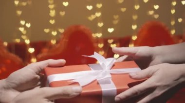 Sevgililer Günü için bir hediye. Eller hediye verir. Kırmızı arka planda, kalpli bir hediye kutusu. Takvime göre, olayın kutlaması 14 Şubat 'ta yapılacak. Kalp atışları..