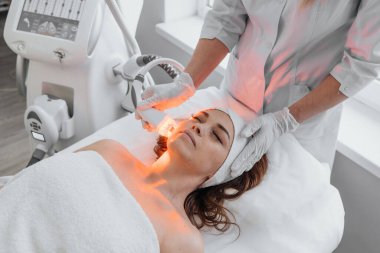 Red LED treatment. Woman doing facial skin therapy. Radiofrequency face lifting. Hardware antiaging procedure. RF lifting and vacuum massage. A cosmetologist performs a cosmetology procedure