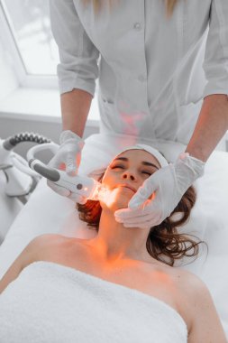 Red LED treatment. Woman doing facial skin therapy. Radiofrequency face lifting. Hardware antiaging procedure. RF lifting and vacuum massage. A cosmetologist performs a cosmetology procedure
