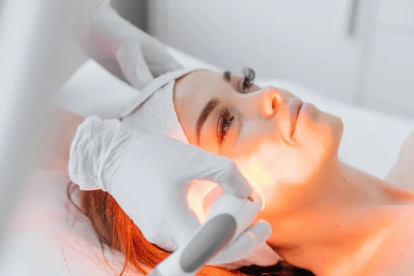 Red LED treatment. Woman doing facial skin therapy. Radiofrequency face lifting. Hardware antiaging procedure. RF lifting and vacuum massage. A cosmetologist performs a cosmetology procedure