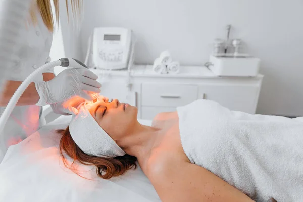 Red LED treatment. Woman doing facial skin therapy. Radiofrequency face lifting. Hardware antiaging procedure. RF lifting and vacuum massage. A cosmetologist performs a cosmetology procedure