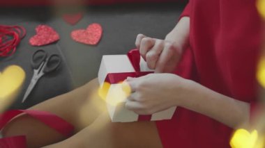 A gift for Valentines Day with your own hands. A girl in a red dress makes a gift for her lover. A box, ribbons, cutting a heart and a festive atmosphere A gift for Valentines Day with your own hands