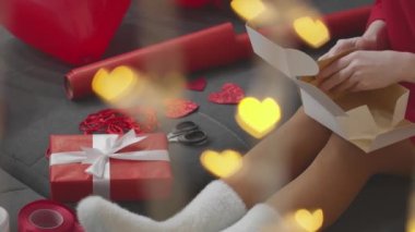 A gift for Valentines Day with your own hands. A girl in a red dress makes a gift for her lover. A box, ribbons, cutting a heart and a festive atmosphere A gift for Valentines Day with your own hands