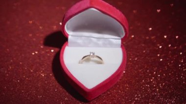 Diamond ring with jewelry gift box on red fabric background. A gold engagement ring for Valentines Day. Wedding proposal marriage concept. Romantic atmosphere of the holiday and decorations.