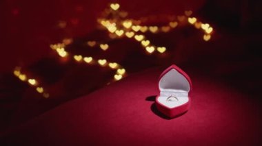 Diamond ring with jewelry gift box on red fabric background. A gold engagement ring for Valentines Day. Wedding proposal marriage concept. Romantic atmosphere of the holiday and decorations.
