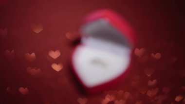 Diamond ring with jewelry gift box on red fabric background. A gold engagement ring for Valentines Day. Wedding proposal marriage concept. Romantic atmosphere of the holiday and decorations.