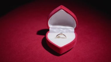 Diamond ring with jewelry gift box on red fabric background. A gold engagement ring for Valentines Day. Wedding proposal marriage concept. Romantic atmosphere of the holiday and decorations.