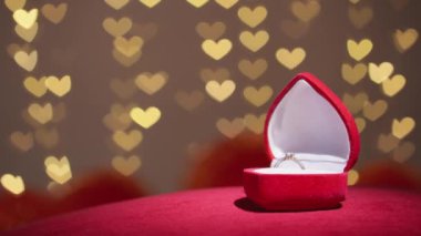 Diamond ring with jewelry gift box on red fabric background. A gold engagement ring for Valentines Day. Wedding proposal marriage concept. Romantic atmosphere of the holiday and decorations.