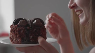A young woman is celebrating her birthday alone. A girl at home with a cake lights candle, makes wish and blows out candle. In black and red clothes, on gray background, holiday celebrates anniversary