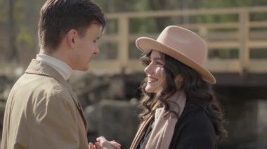 Young couple on walk in park in the spring. A romantic meeting of a happy boy and girl on vacation in the forest. Love and relationship between a man and a woman. Smiles, hugs by the bridge