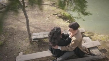 Young couple on walk in park in the spring. A romantic meeting of a happy boy and girl on vacation in the forest. Love and relationship between a man and a woman. Smiles, hugs on the bench