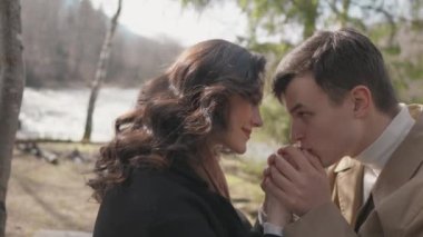 Young couple on walk in park in the spring. A romantic meeting of a happy boy and girl on vacation in the forest. Love and relationship between a man and a woman. Smiles, hugs and emotions by river