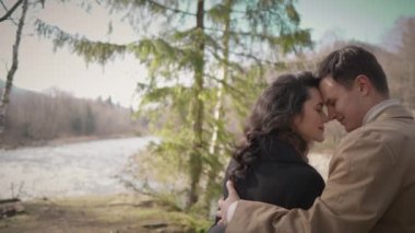 Young couple on walk in park in the spring. A romantic meeting of a happy boy and girl on vacation in the forest. Love and relationship between a man and a woman. Smiles, hugs and emotions by river
