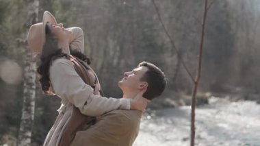 Young couple on walk in park in the spring. A romantic meeting of a happy boy and girl on vacation in the forest. Love and relationship between a man and a woman. Smiles, hugs and emotions by river