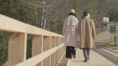 Boy and girl running on wooden bridge over river in mountains. Happy carefree young couple man and woman having fun, romantically and actively resting, joyfully spending time together in relationship.