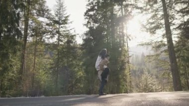 Romantic couple walking along highway in mountains forest. Man takes woman hand and romantic date outdoors. Joyful people boy and girl sit, walk on road. Love couple having fun while walking in nature