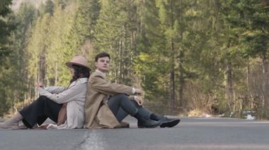 Romantic couple walking along highway in mountains forest. Man takes woman hand and romantic date outdoors. Joyful people boy and girl sit, walk on road. Love couple having fun while walking in nature