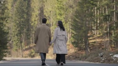Romantic couple walking along highway in mountains forest. Man takes woman hand and romantic date outdoors. Joyful people boy and girl sit, walk on road. Love couple having fun while walking in nature