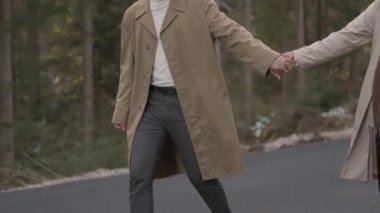 Romantic couple walking along highway in mountains forest. Man takes woman hand and romantic date outdoors. Joyful people boy and girl sit, walk on road. Love couple having fun while walking in nature