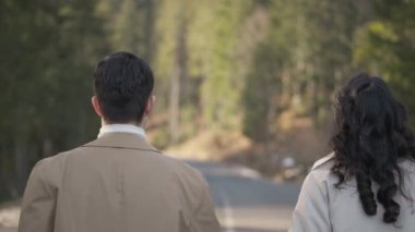 Romantic couple walking along highway in mountains forest. Man takes woman hand and romantic date outdoors. Joyful people boy and girl sit, walk on road. Love couple having fun while walking in nature