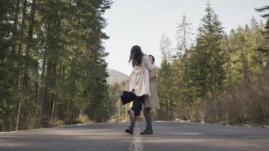Romantic couple walking along highway in mountains forest. Man takes woman hand and romantic date outdoors. Joyful people boy and girl sit, walk on road. Love couple having fun while walking in nature