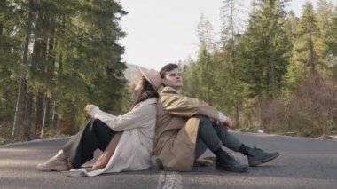 Romantic couple walking along highway in mountains forest. Man takes woman hand and romantic date outdoors. Joyful people boy and girl sit, walk on road. Love couple having fun while walking in nature