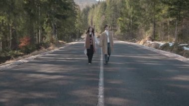 Romantic couple walking along highway in mountains forest. Man takes woman hand and romantic date outdoors. Joyful people boy and girl sit, walk on road. Love couple having fun while walking in nature