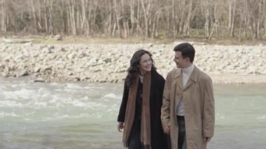 Joyful young couple flirt near river in park. Girl and boy resting in nature. Happy man woman in forest having fun, spending time together. Concept relationship, love, dating in spring, summer, autumn