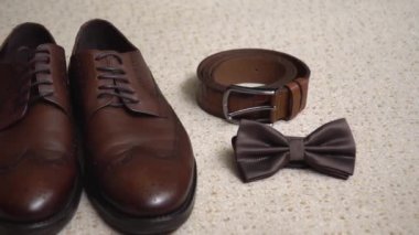 Erkekler halıda kahverengi deri ayakkabılar. Kompozisyon: Ayakkabılar, kemer, kelebek. Damadın sabah toplantısı, düğün hazırlıkları. Erkekler için ayakkabılar.