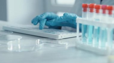 Bir kadın araştırmacı, bir laboratuarda, kişisel bilgisayar monitörünün arkasında oturuyor. Arkaplan araştırma istatistiklerine karşı. Korumada çalışan ilaç uzmanı klavyede çalışıyor..