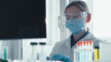 Bir kadın araştırmacı, bir laboratuarda, kişisel bilgisayar monitörünün arkasında oturuyor. Arkaplan araştırma istatistiklerine karşı. Korumada çalışan ilaç uzmanı klavyede çalışıyor..