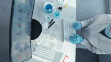 Bir kadın araştırmacı, bir laboratuarda, kişisel bilgisayar monitörünün arkasında oturuyor. Arkaplan araştırma istatistiklerine karşı. Korumada çalışan ilaç uzmanı klavyede çalışıyor..