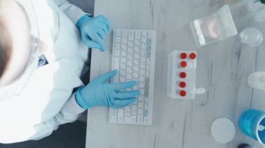 Bir kadın araştırmacı, bir laboratuarda, kişisel bilgisayar monitörünün arkasında oturuyor. Arkaplan araştırma istatistiklerine karşı. Korumada çalışan ilaç uzmanı klavyede çalışıyor..