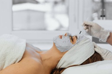 Güzellik salonunda yüz için kozmetik maske. Spa prosedürleri, rahatlama ve cilt bakımı. Bir kadın güzellik salonundaki bir kozmetikçiden yüz bakımı alır..