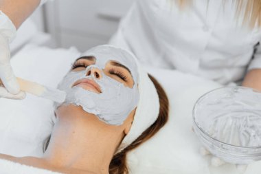 Güzellik salonunda yüz için kozmetik maske. Spa prosedürleri, rahatlama ve cilt bakımı. Bir kadın güzellik salonundaki bir kozmetikçiden yüz bakımı alır..
