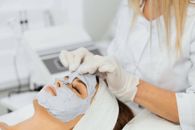 Güzellik salonunda yüz için kozmetik maske. Spa prosedürleri, rahatlama ve cilt bakımı. Bir kadın güzellik salonundaki bir kozmetikçiden yüz bakımı alır..
