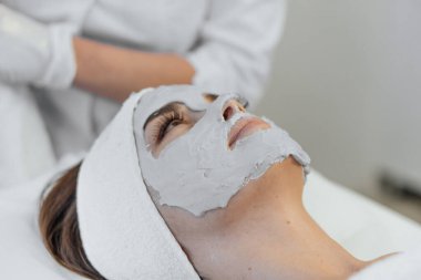 Güzellik salonunda yüz için kozmetik maske. Spa prosedürleri, rahatlama ve cilt bakımı. Bir kadın güzellik salonundaki bir kozmetikçiden yüz bakımı alır..