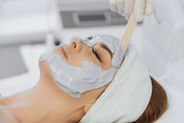 Cosmetic beauty mask for face in beauty salon. Spa procedures, relaxation and skin care. A woman receives facial care from a cosmetologist in a spa salon.