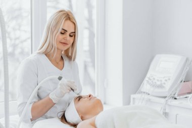 Radiofrequency facial skin lifting. Hardware cosmetology RF lifting procedure and hardware facial massage. Rejuvenation, skin care in a beauty salon. Woman doctor cosmetologist and girl in spa clinic.